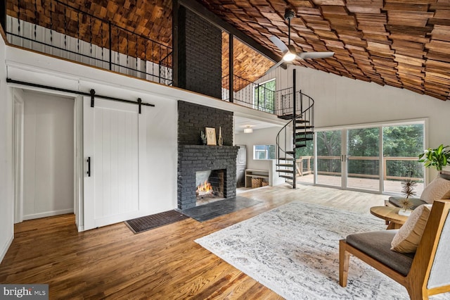 living room with high vaulted ceiling, a barn door, wood finished floors, stairs, and a brick fireplace