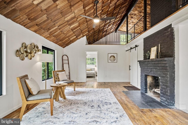 living area with a barn door, a ceiling fan, wood ceiling, wood finished floors, and high vaulted ceiling