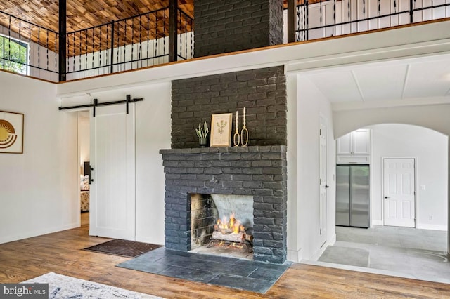 unfurnished living room with a barn door, arched walkways, a towering ceiling, wood finished floors, and a fireplace