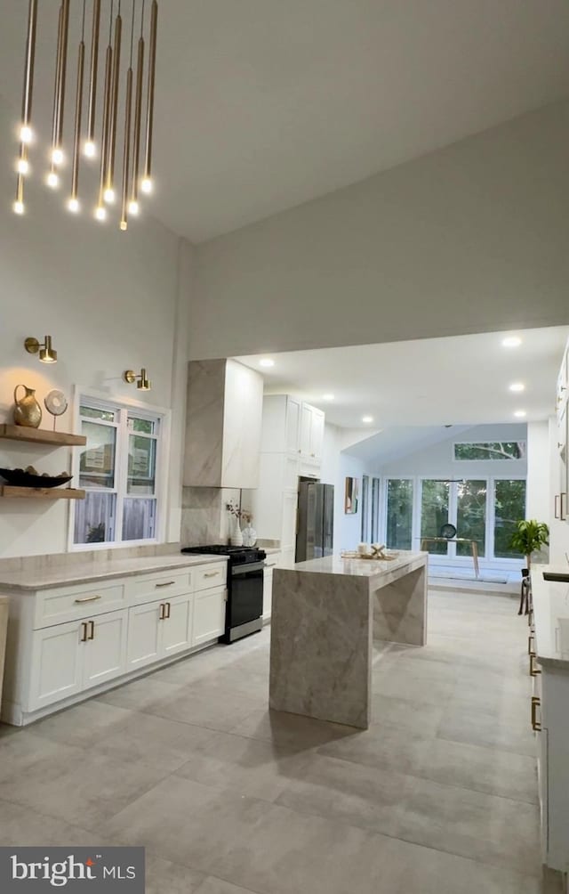 kitchen featuring white cabinets, a kitchen island, freestanding refrigerator, and range with gas stovetop