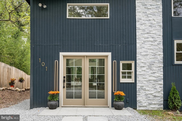 view of exterior entry featuring stone siding, fence, and french doors