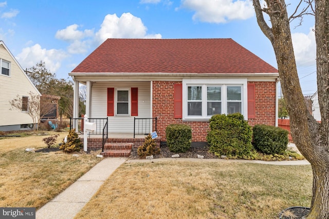 bungalow featuring brick siding, a porch, a front lawn, and roof with shingles