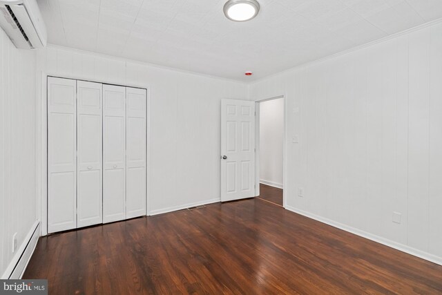 unfurnished bedroom with a baseboard heating unit, a closet, dark wood-style flooring, and a wall unit AC