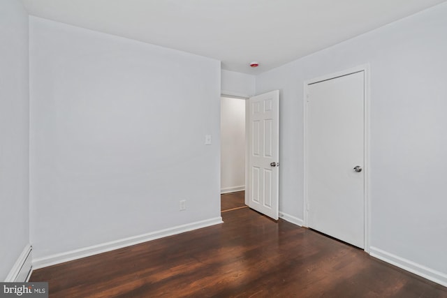 unfurnished bedroom featuring a baseboard heating unit, wood finished floors, and baseboards