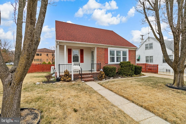 view of front of home with brick siding, covered porch, a front yard, and fence