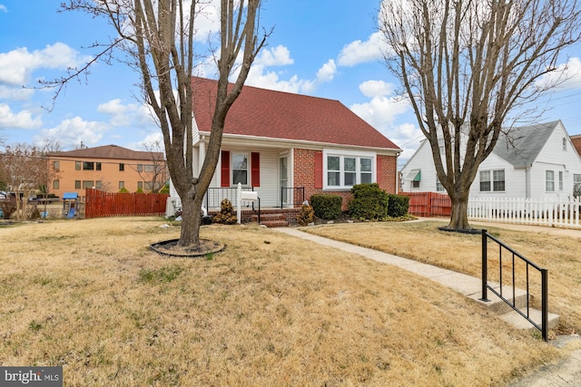 view of front of house featuring brick siding, a porch, a front yard, and fence