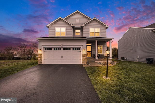 traditional-style house featuring an attached garage, covered porch, stone siding, a yard, and driveway