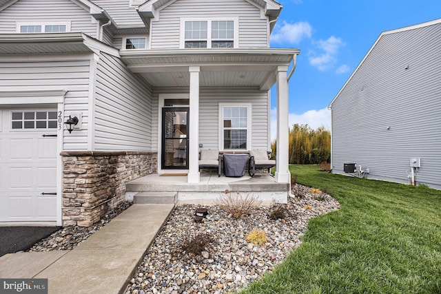 doorway to property featuring stone siding, covered porch, a lawn, and an attached garage