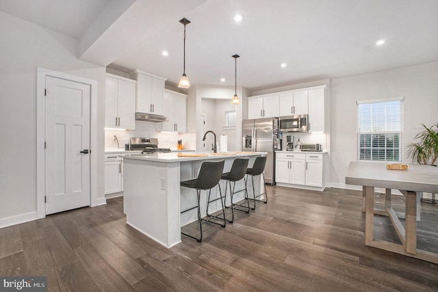 kitchen featuring appliances with stainless steel finishes, dark wood-style flooring, a kitchen island with sink, and under cabinet range hood