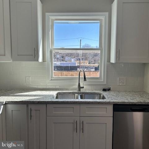 kitchen featuring light stone counters, backsplash, stainless steel dishwasher, white cabinetry, and a sink