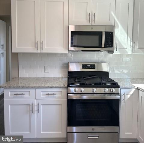 kitchen featuring stainless steel appliances, light stone counters, white cabinetry, and decorative backsplash