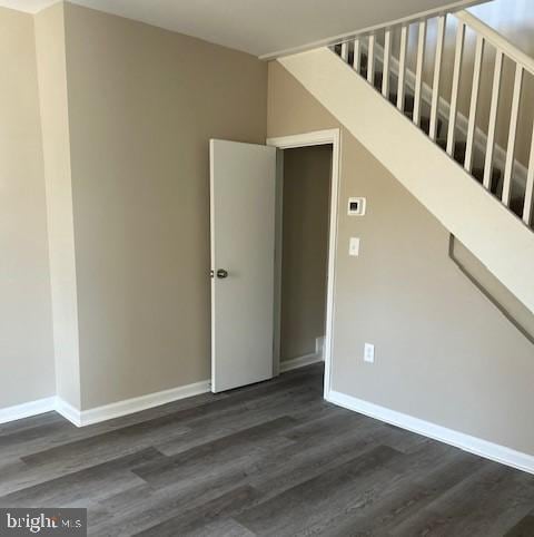 empty room featuring stairs, dark wood finished floors, and baseboards