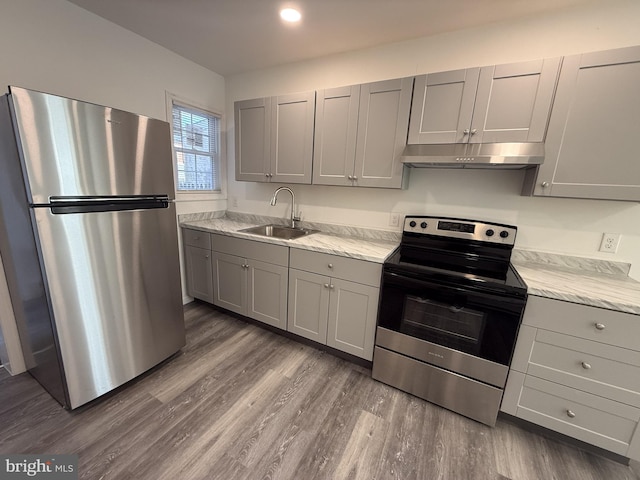 kitchen with appliances with stainless steel finishes, gray cabinets, a sink, and under cabinet range hood