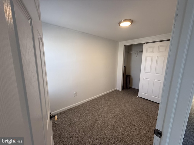 unfurnished bedroom featuring baseboards, dark colored carpet, and a closet