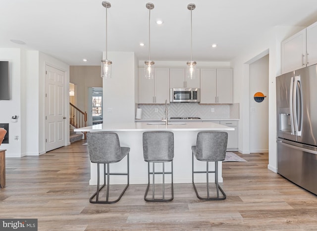 kitchen with stainless steel appliances, a kitchen bar, light countertops, and light wood-style floors