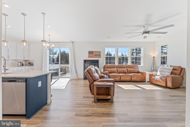 living area featuring ceiling fan with notable chandelier, light wood finished floors, and baseboards