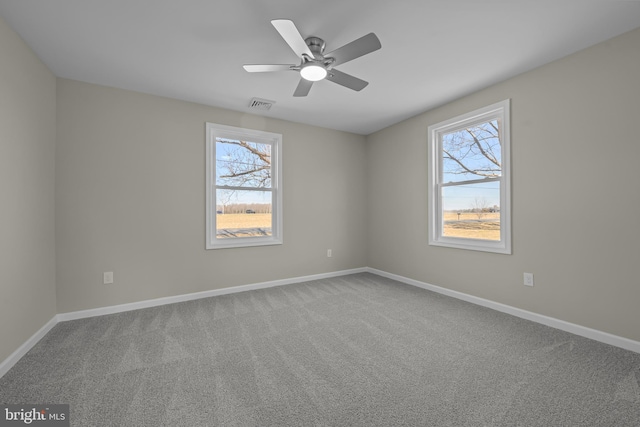 carpeted empty room with baseboards, visible vents, and a ceiling fan