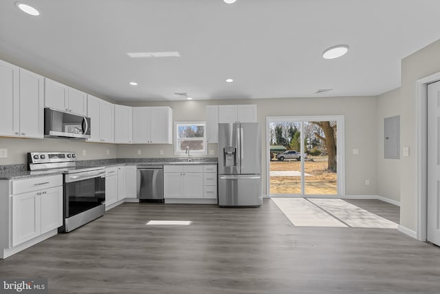 kitchen featuring dark wood-style floors, appliances with stainless steel finishes, white cabinets, a sink, and electric panel