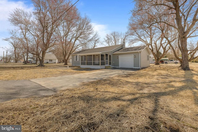 ranch-style home featuring a sunroom, a chimney, an attached garage, and concrete driveway