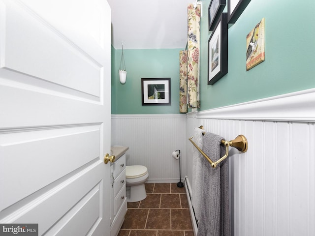 bathroom with a baseboard radiator, wainscoting, vanity, and toilet