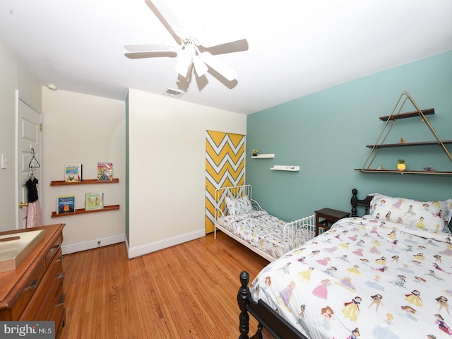 bedroom featuring light wood-style flooring, a ceiling fan, visible vents, and baseboards