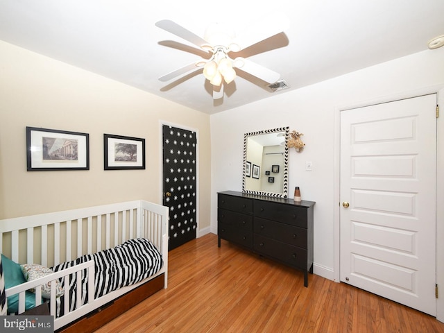 bedroom featuring ceiling fan, wood finished floors, visible vents, baseboards, and a nursery area