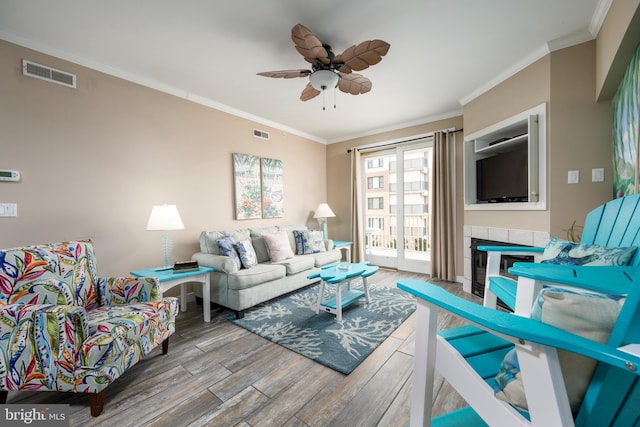 living room with ornamental molding, a tiled fireplace, wood finished floors, and visible vents