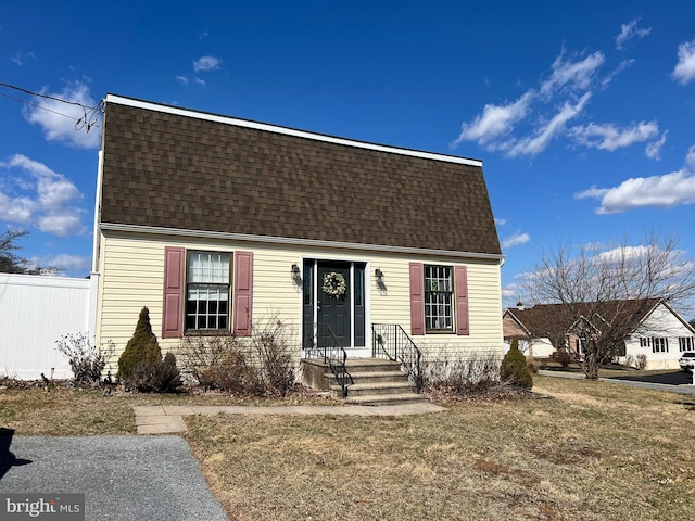 colonial inspired home with a front lawn, roof with shingles, and fence