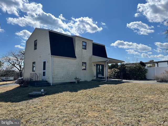 rear view of property featuring a yard, fence, and a gambrel roof