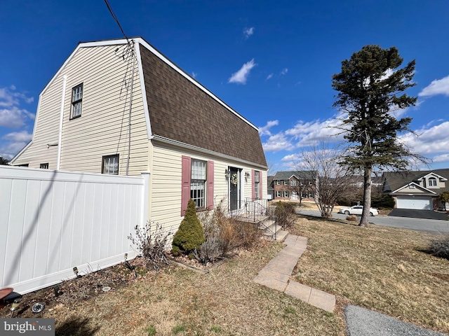 view of side of home featuring roof with shingles, fence, and a gambrel roof