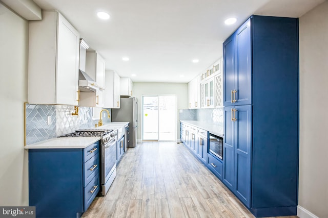 kitchen featuring light wood finished floors, blue cabinetry, stainless steel appliances, light countertops, and wall chimney exhaust hood