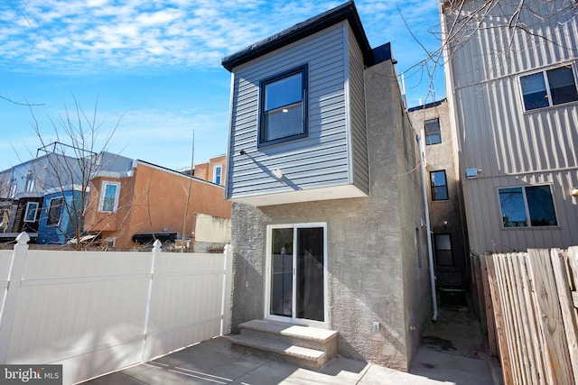 back of house with stucco siding, entry steps, and fence