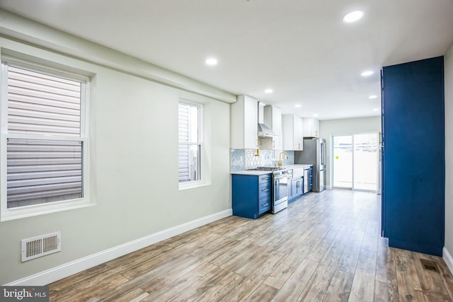 kitchen featuring visible vents, backsplash, stainless steel appliances, light wood finished floors, and light countertops