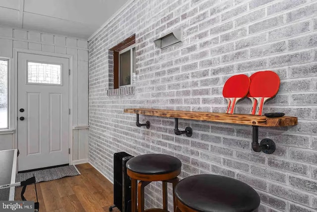 foyer entrance with wood finished floors and brick wall