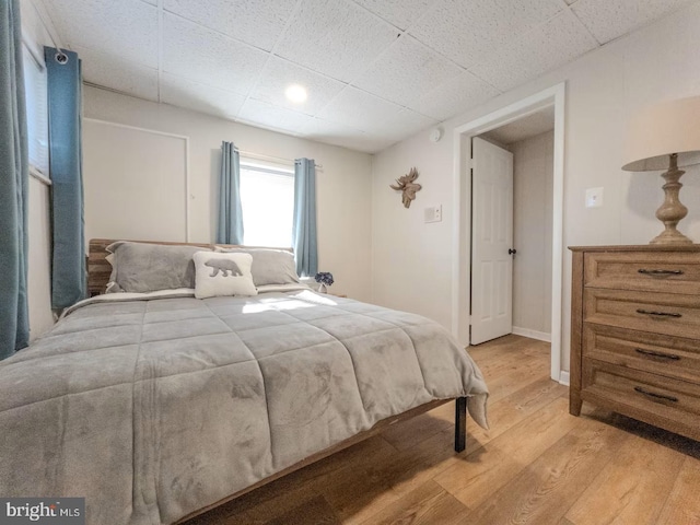 bedroom featuring a drop ceiling, baseboards, and light wood-style floors