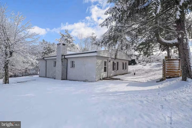 snow covered property with stucco siding and a chimney