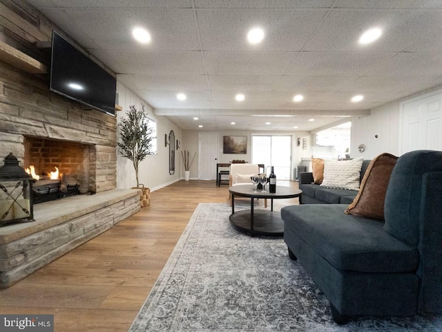 living room featuring baseboards, a paneled ceiling, a stone fireplace, and wood finished floors