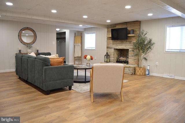 living area with a stone fireplace, wood finished floors, visible vents, and baseboards