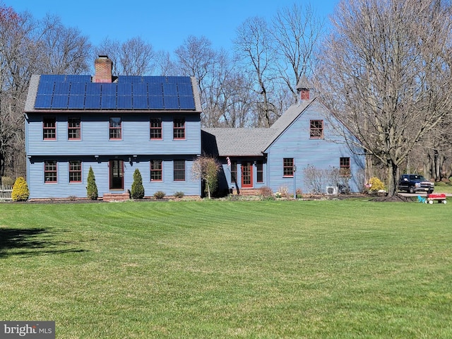 colonial inspired home featuring a chimney, solar panels, and a front yard