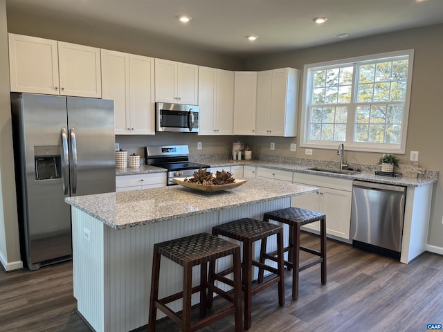 kitchen with stainless steel appliances, dark wood-style flooring, a kitchen island, a sink, and white cabinets