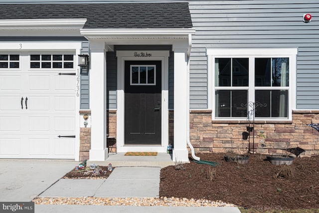 property entrance featuring stone siding, an attached garage, and roof with shingles