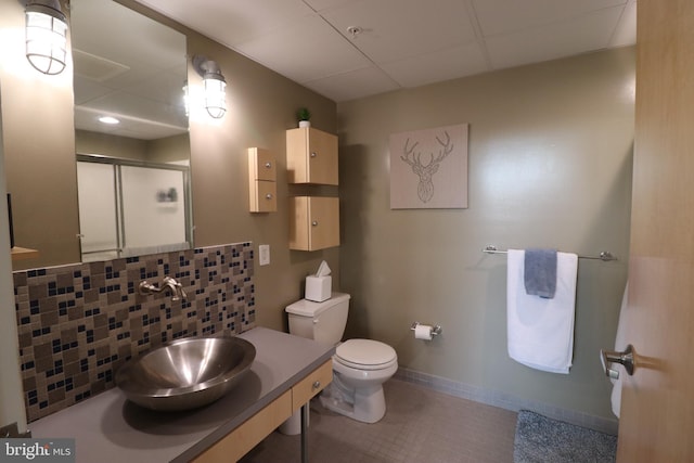 full bathroom featuring toilet, a sink, tasteful backsplash, a shower stall, and baseboards