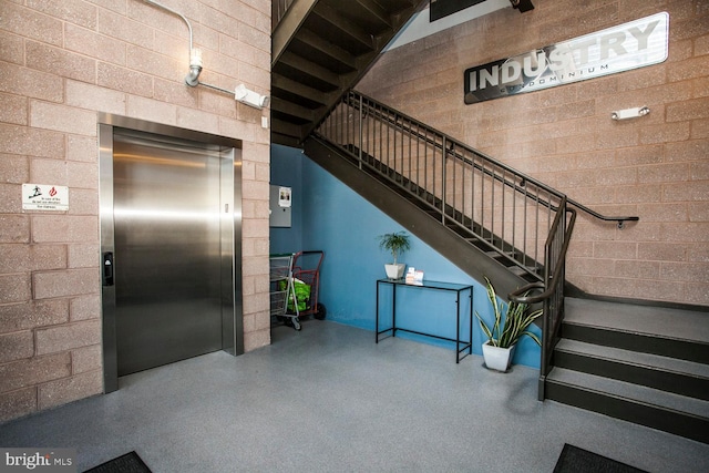 stairs featuring elevator, concrete block wall, and speckled floor