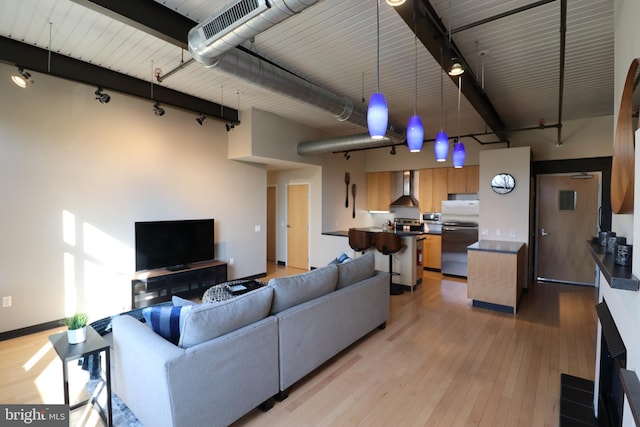 living room featuring track lighting, a high ceiling, visible vents, and light wood-type flooring