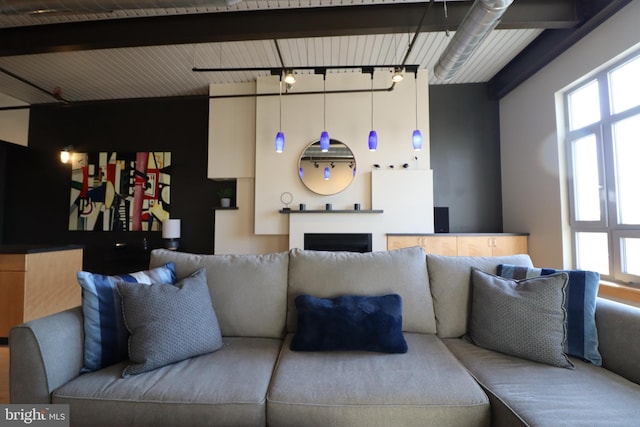 living room with rail lighting, beam ceiling, and a fireplace