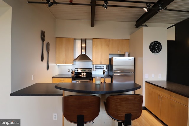 kitchen featuring dark countertops, beamed ceiling, appliances with stainless steel finishes, and wall chimney exhaust hood