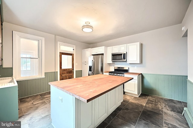 kitchen featuring wooden counters, a wainscoted wall, white cabinets, stainless steel appliances, and a baseboard radiator