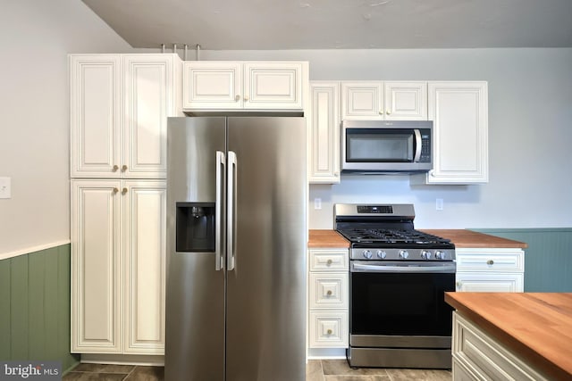 kitchen with a wainscoted wall, white cabinets, butcher block counters, and stainless steel appliances