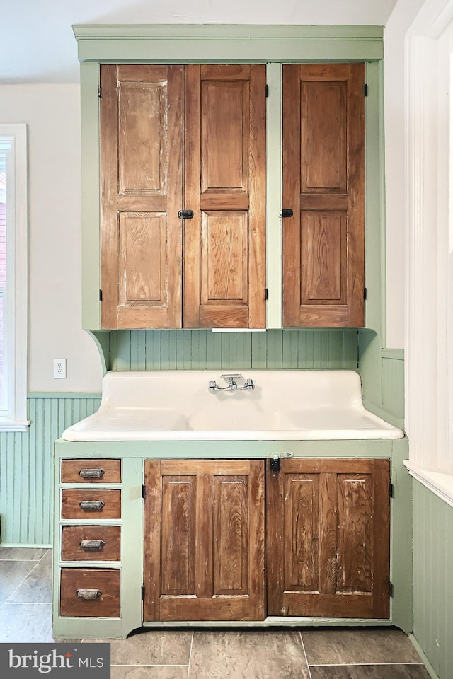 kitchen with a wainscoted wall, brown cabinetry, and light countertops