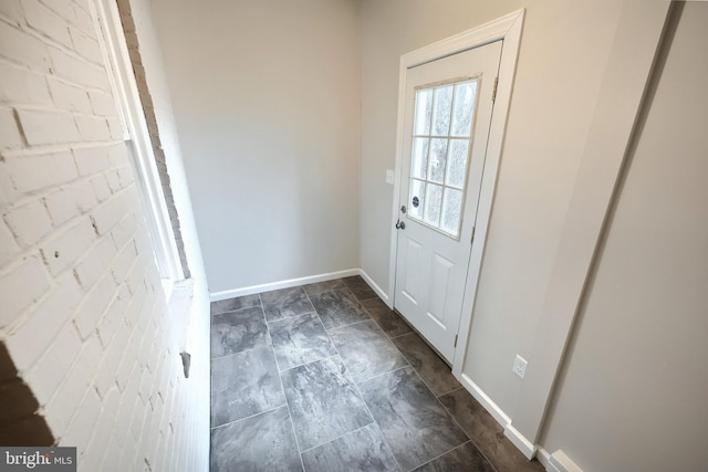 doorway with baseboards and brick wall